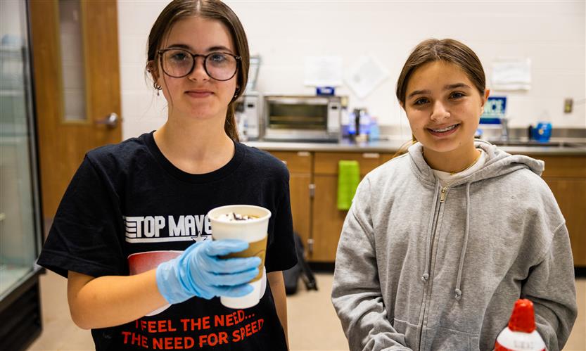 Two girls smile while holding a cup of coffee